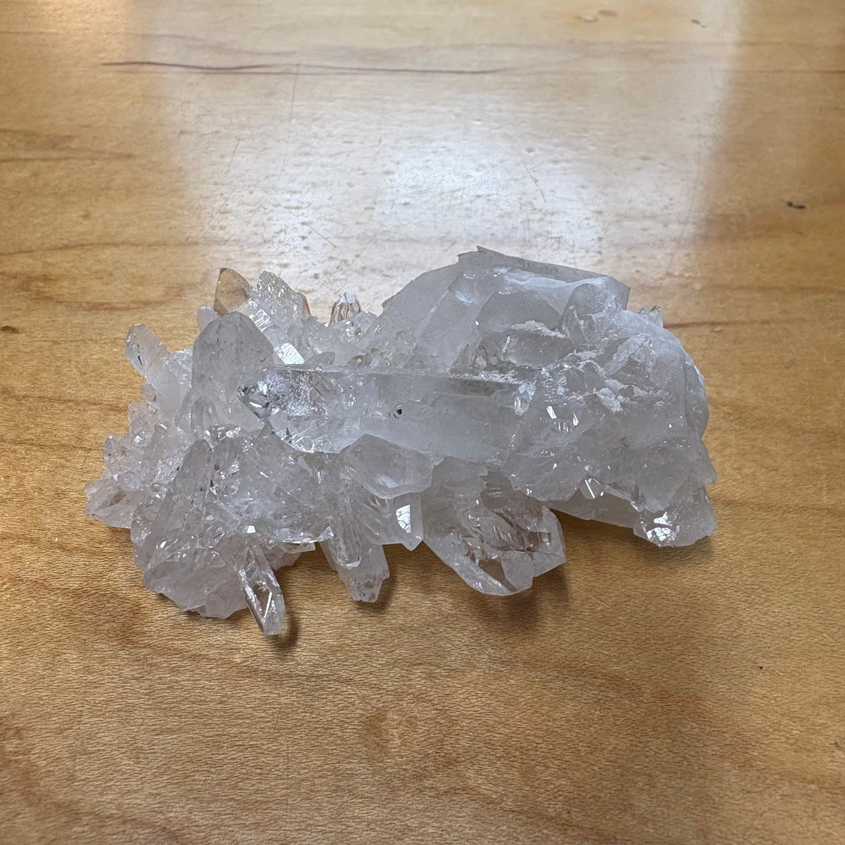 A cluster of clear quartz crystal points resting on a light brown wooden tabletop.