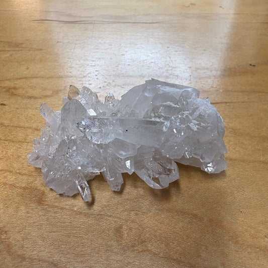 A cluster of clear quartz crystal points resting on a light brown wooden tabletop.