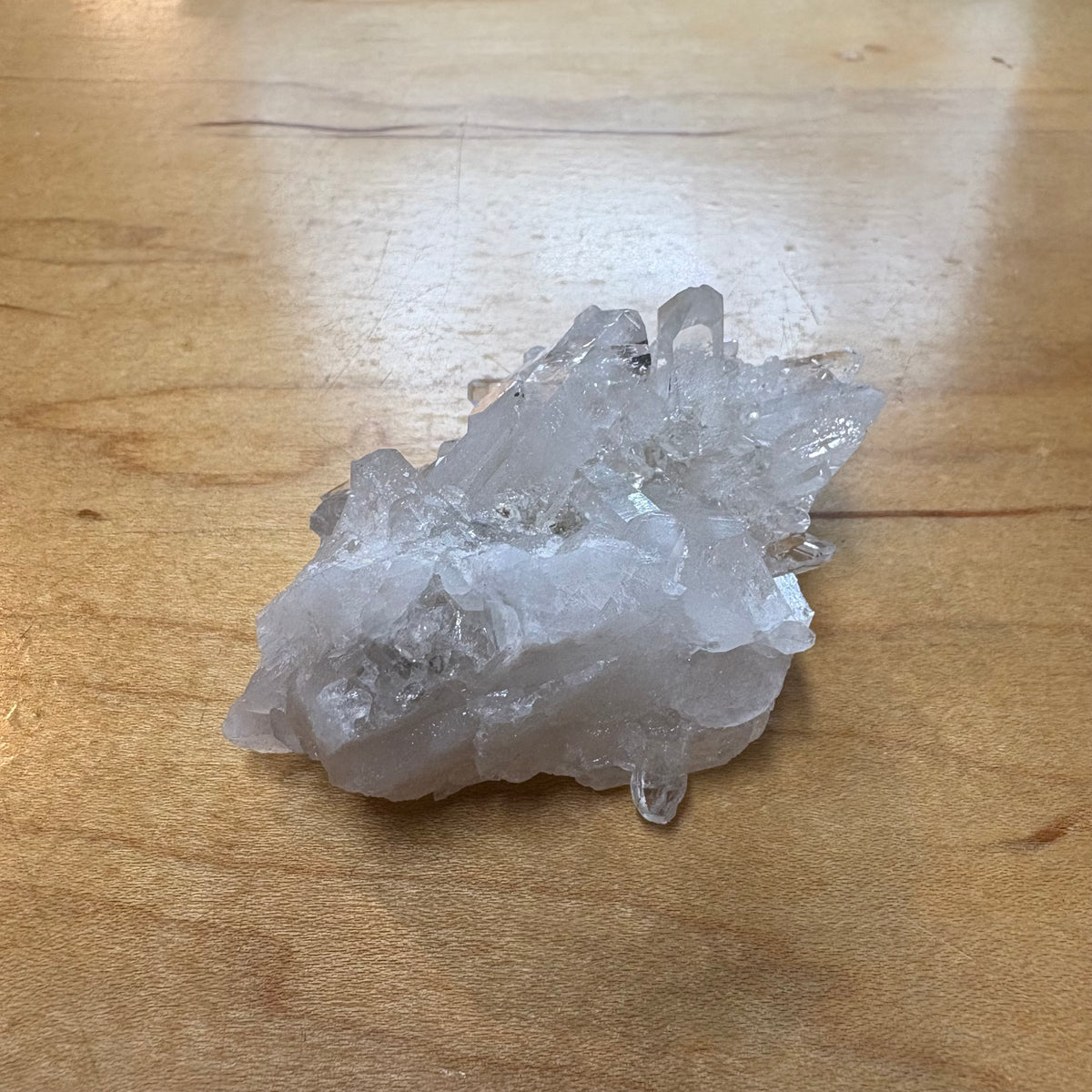 A raw white crystal cluster with rough, jagged edges resting on a light brown wooden tabletop.