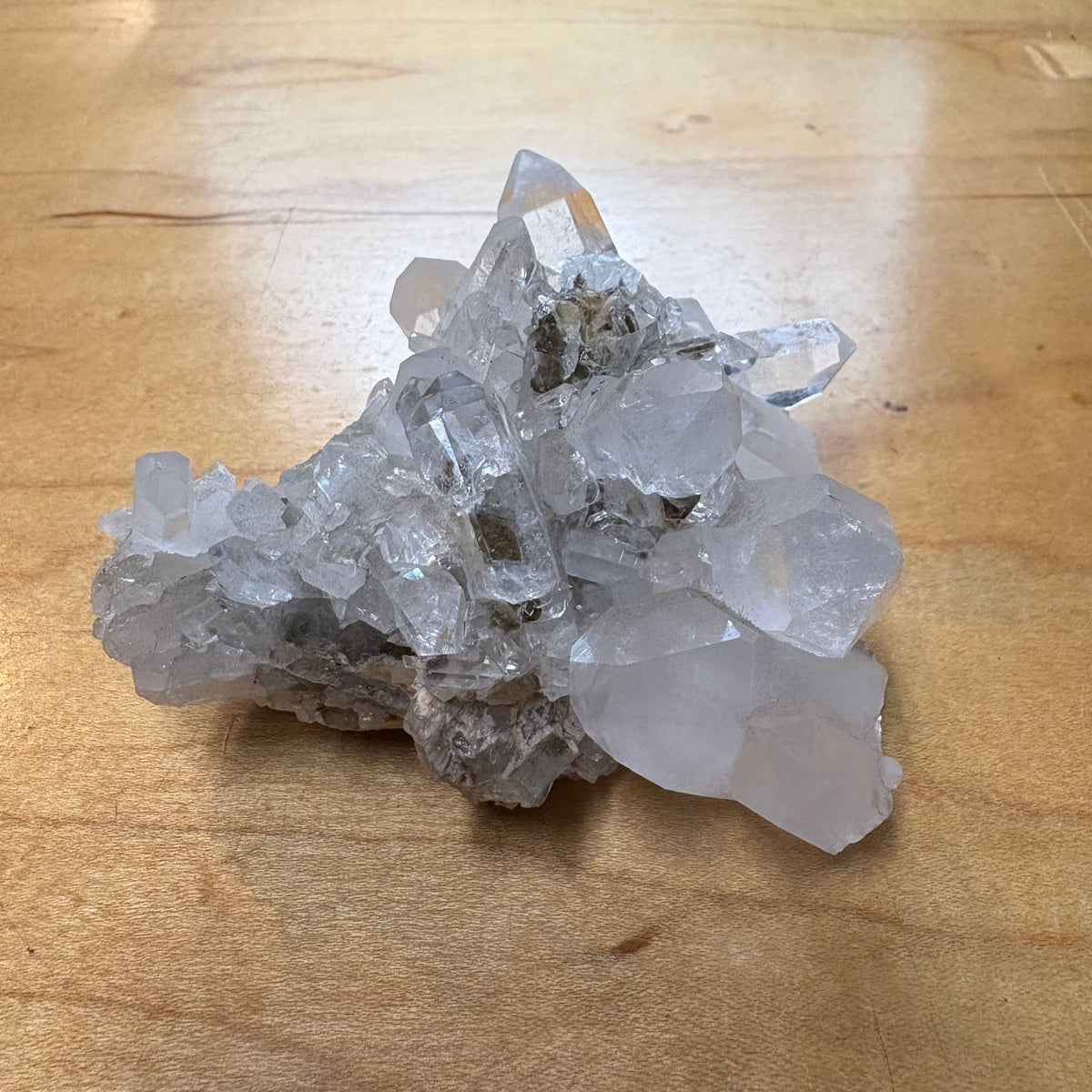 A natural clear quartz crystal cluster with multiple sharp points resting on a light brown wooden surface.