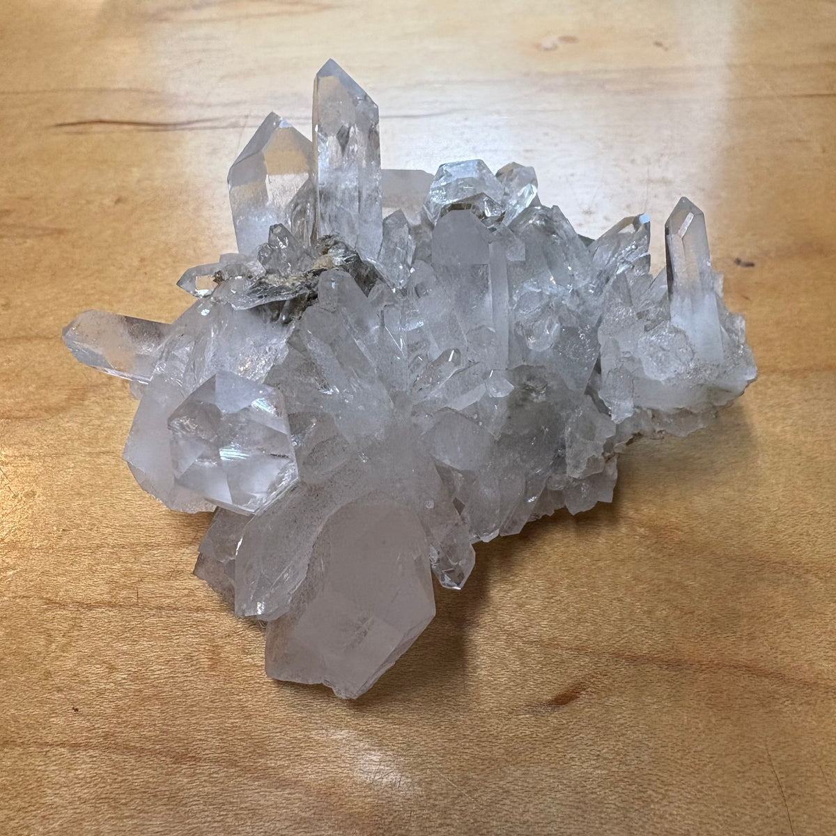 A cluster of natural clear quartz crystal points resting on a light brown wooden surface.