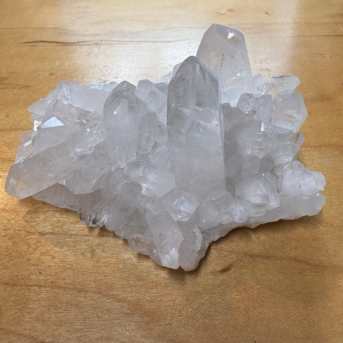 A cluster of natural clear quartz crystal points resting on a light brown wooden surface.