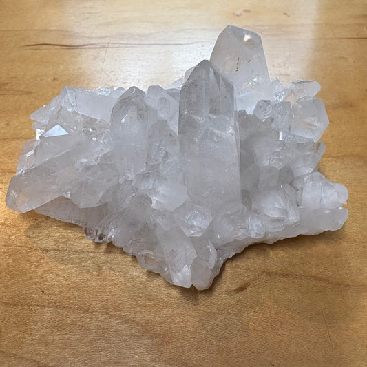 A cluster of natural clear quartz crystal points resting on a light brown wooden surface.