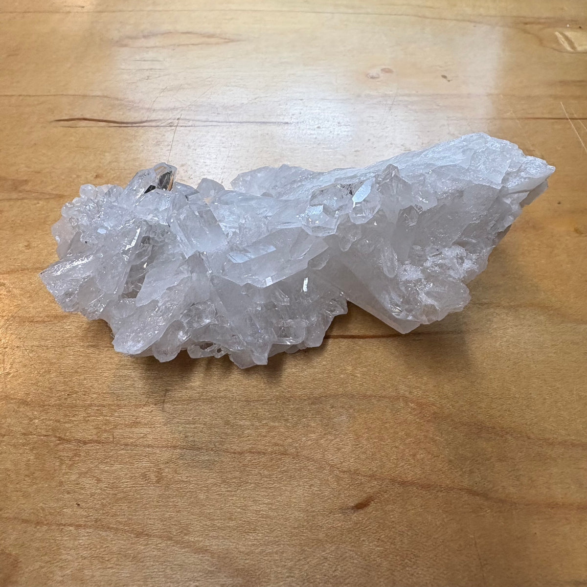 A raw, translucent white crystal cluster with sharp natural edges, resting on a light brown wooden surface.