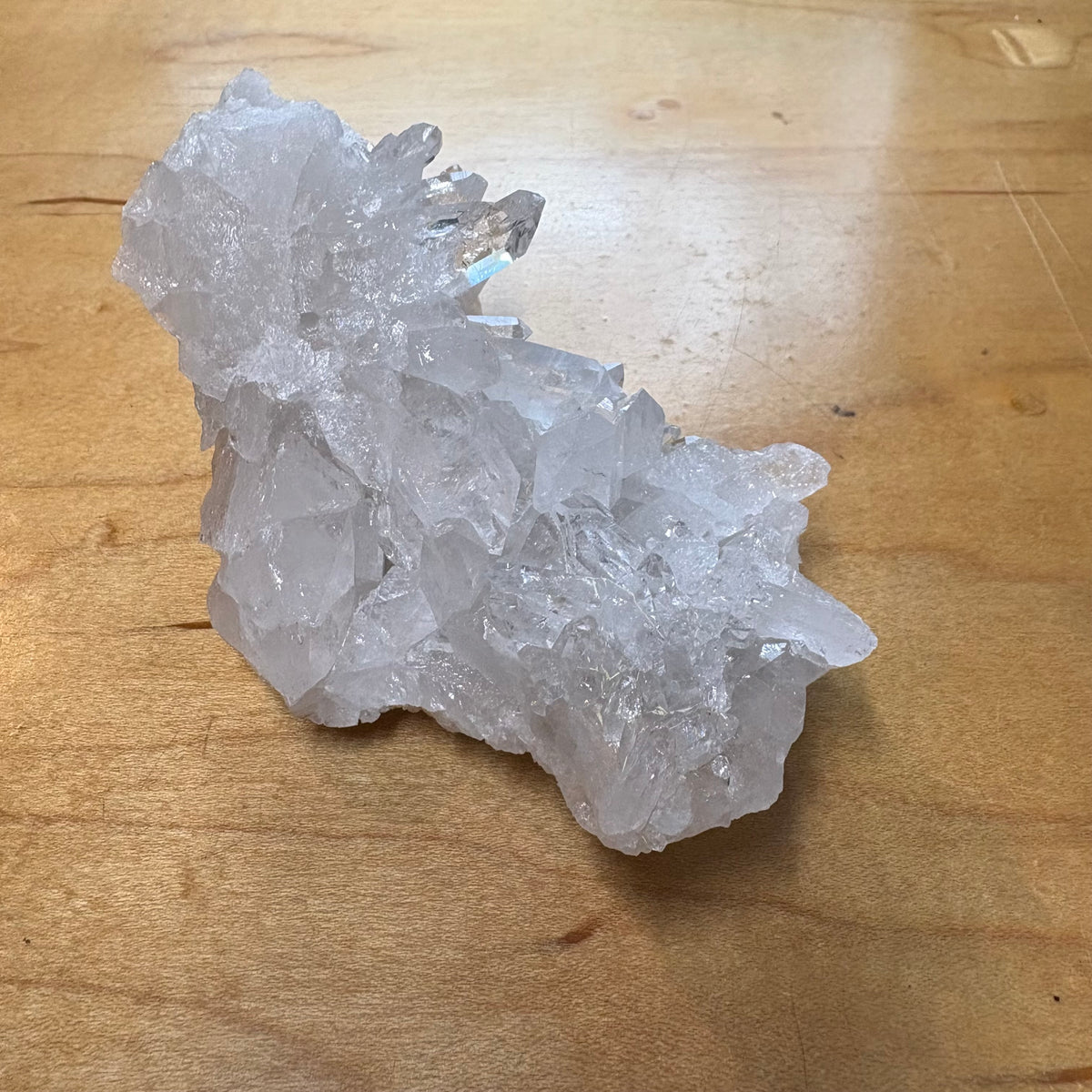 A raw crystal cluster with translucent white to light gray quartz-like points, photographed on a warm wood tabletop.