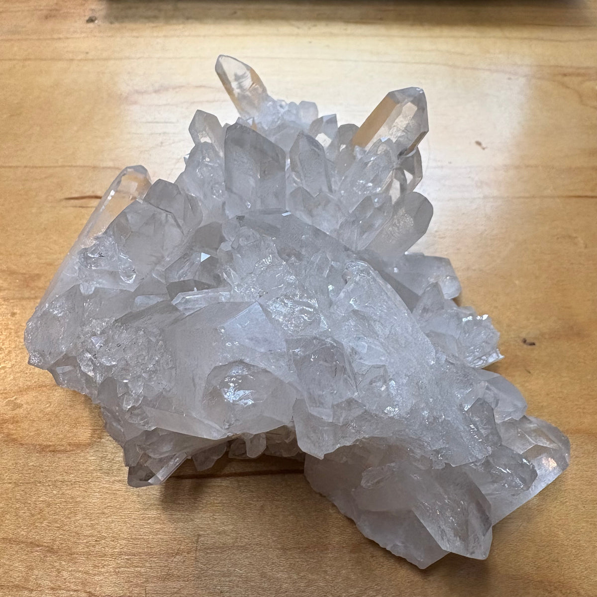 A cluster of natural clear quartz crystal points resting on a light brown wooden surface.