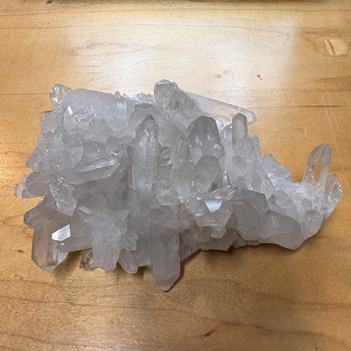 A cluster of natural clear quartz crystal points resting on a light brown wooden tabletop.