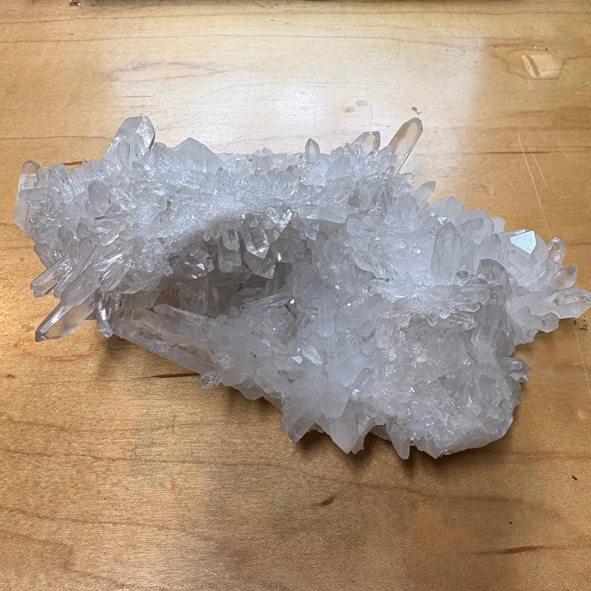 A cluster of clear quartz crystal points resting on a light brown wooden surface.