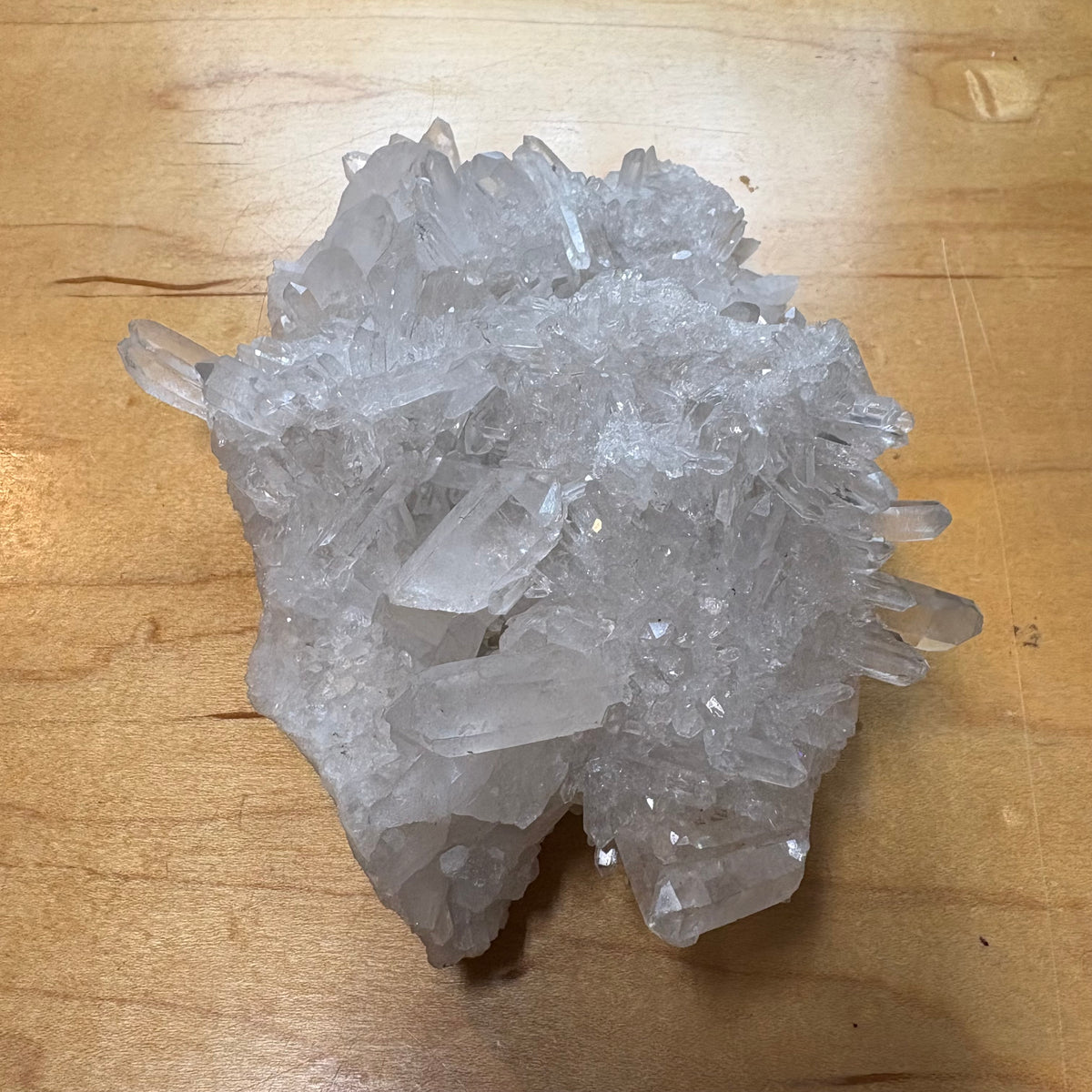 A cluster of clear quartz crystal points resting on a light brown wooden surface.