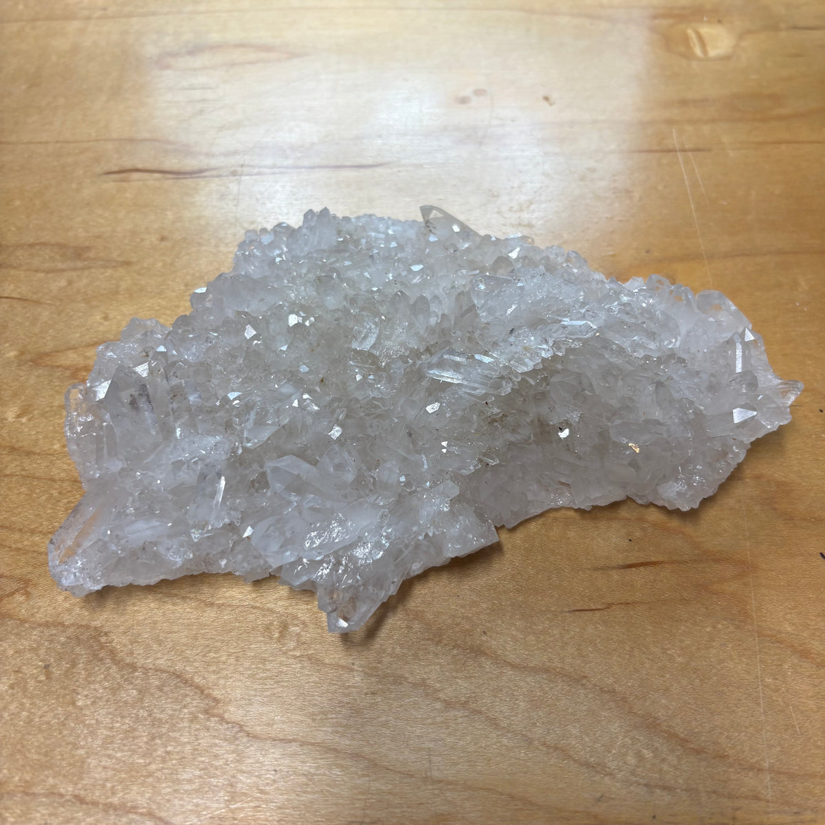 A cluster of clear, translucent crystals resting on a light brown wooden surface.