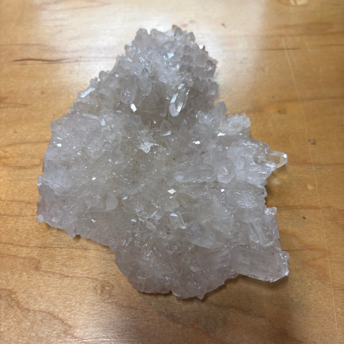 A raw crystal cluster with translucent white to light gray crystalline structure, photographed on a wooden tabletop.