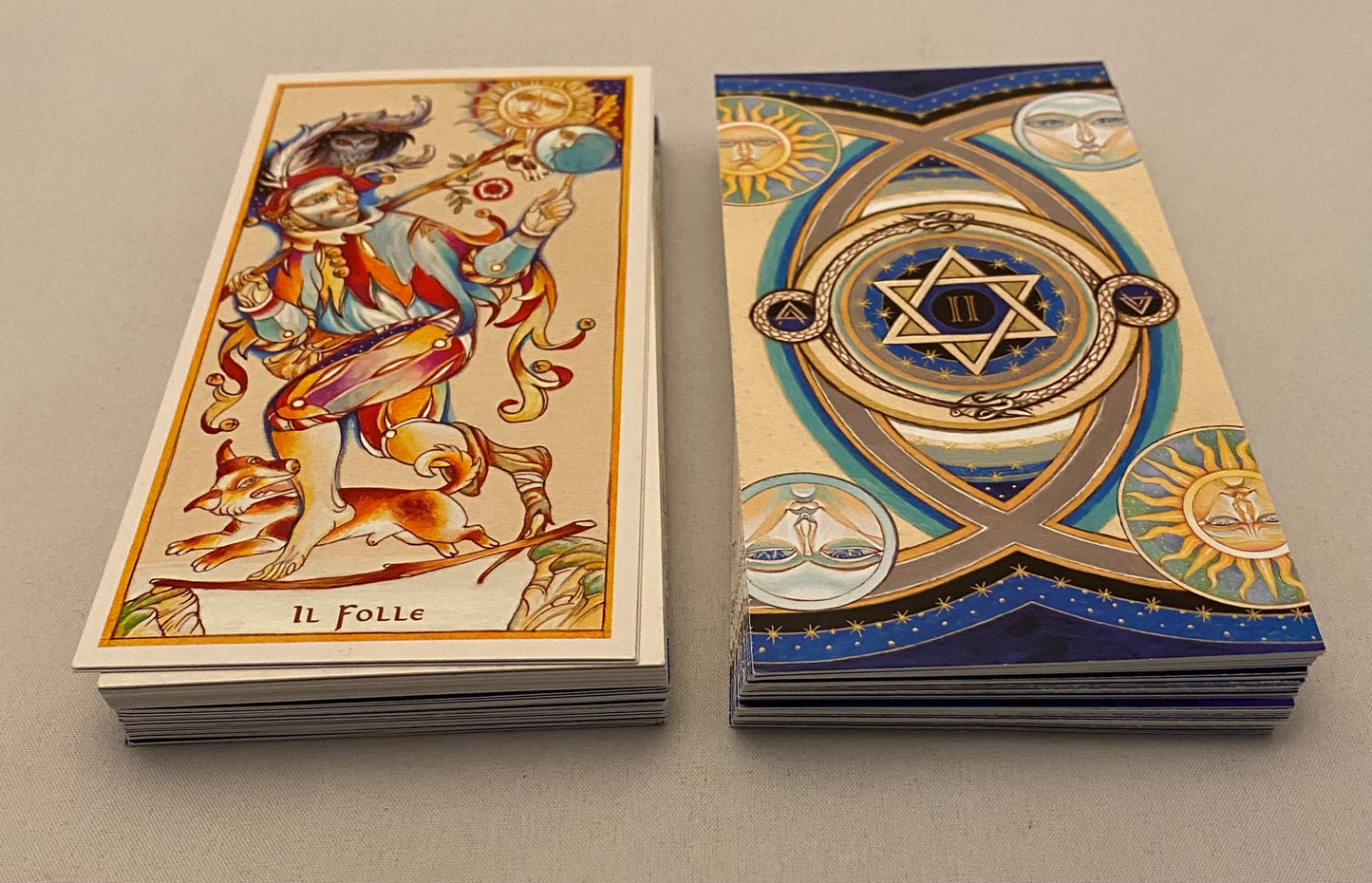 Two tarot cards from a deck with intricate designs on a gray background