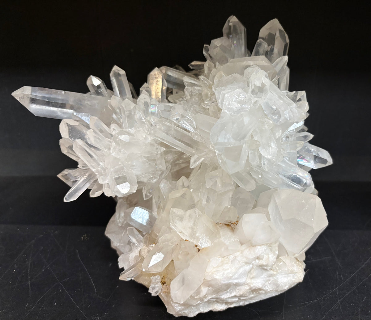 A natural quartz crystal cluster specimen with multiple clear, faceted quartz points rising from an off-white matrix, photographed against a solid black background.