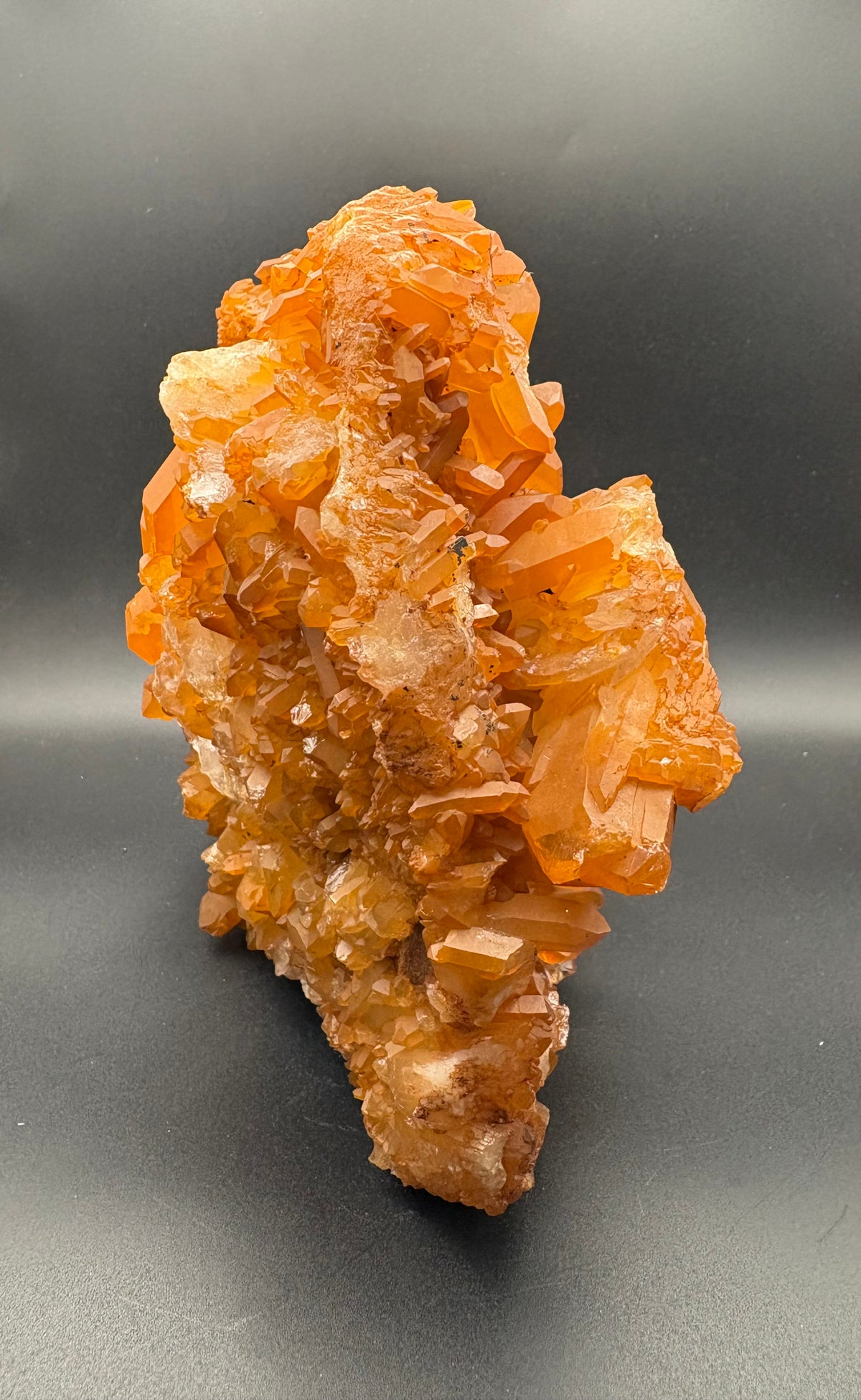 A natural Tangerine Quartz crystal cluster specimen with multiple faceted translucent crystal points on a dark gray background.