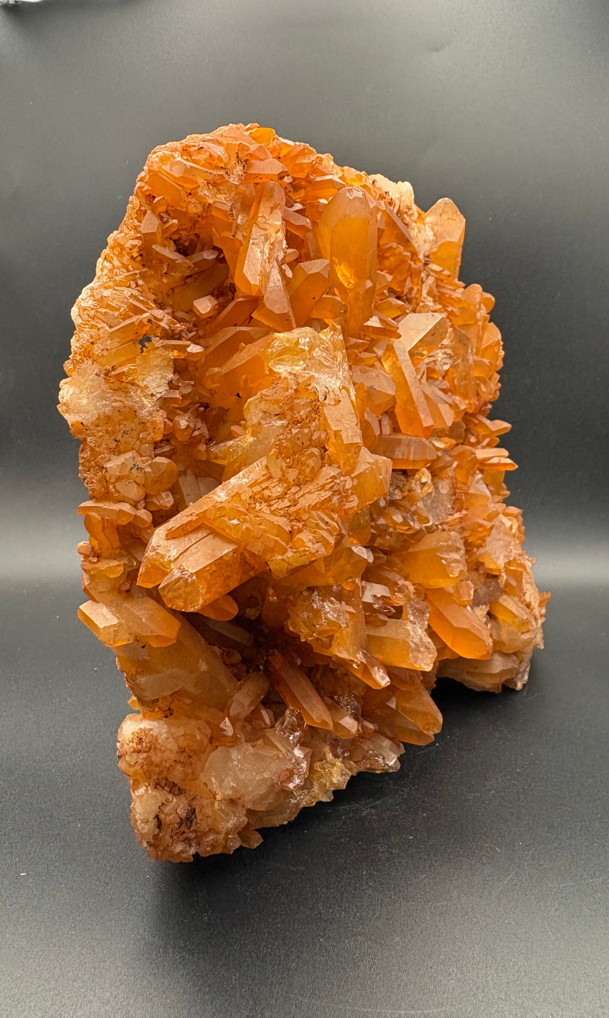 A natural Tangerine Quartz crystal cluster specimen with multiple faceted translucent crystal points on a dark gray background.