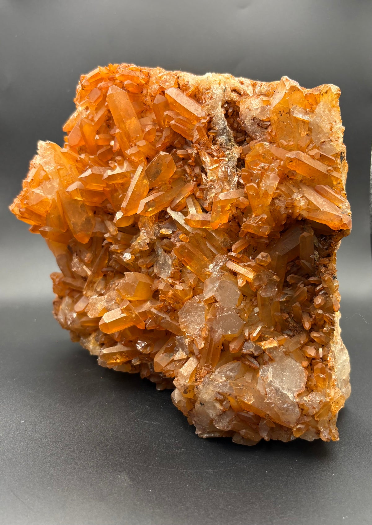 A natural Tangerine Quartz crystal cluster specimen with multiple faceted translucent crystal points on a dark gray background.