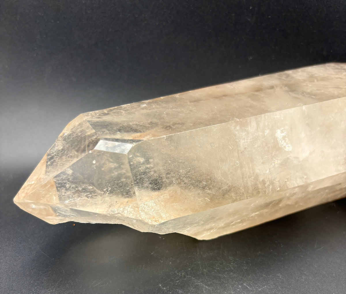 A natural smoky quartz crystal point with subtle golden-brown inclusions, photographed on a dark gray background.