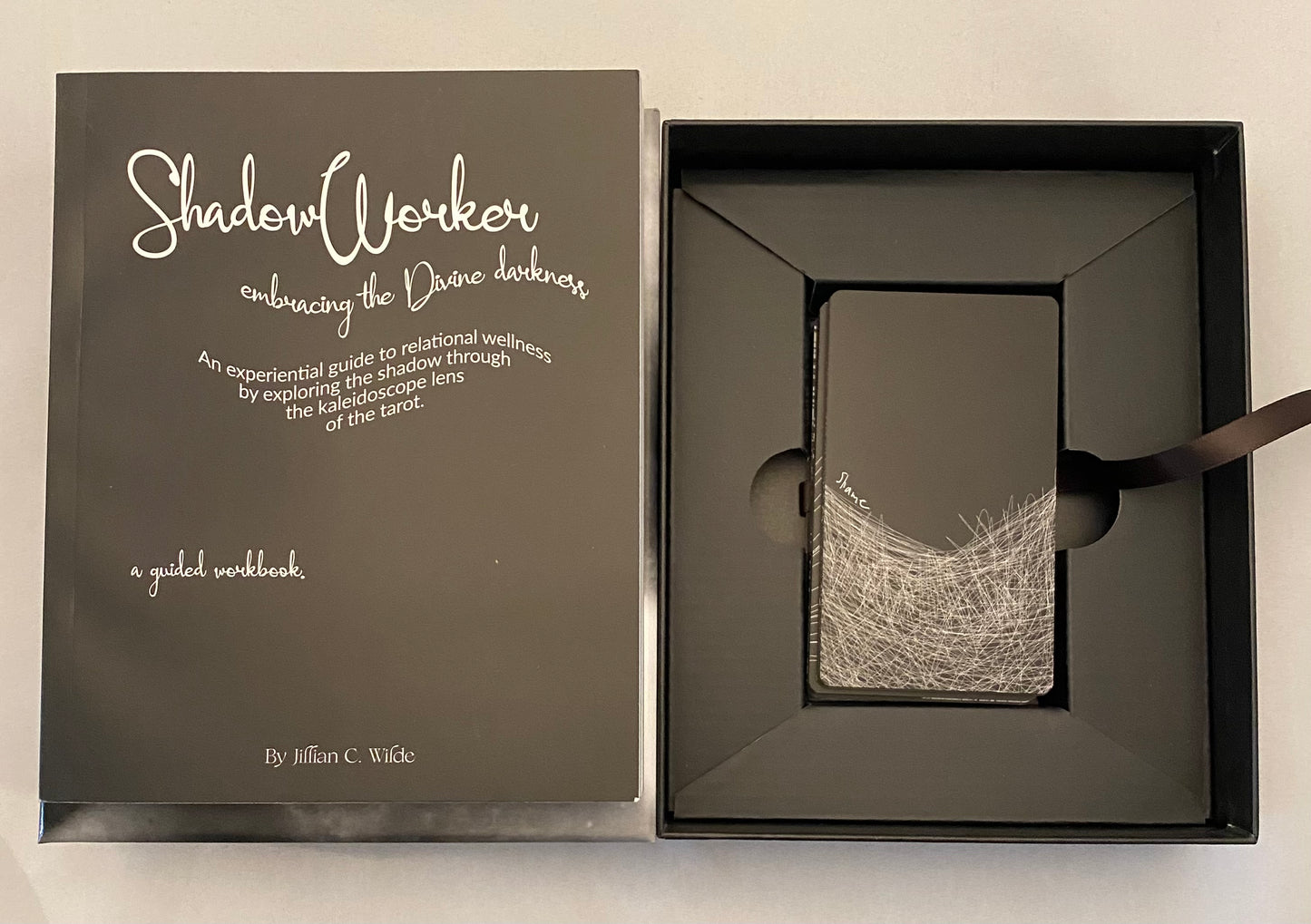 Tarot deck and Dark gray workbook titled 'Shadow Worker' with a black ribbon in an open box on a beige background