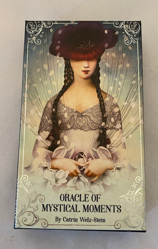 Cardboard box with an illustration of a woman and text 'Oracle of Mystical Moments' by Catrin Welz-Stein on a gray background.