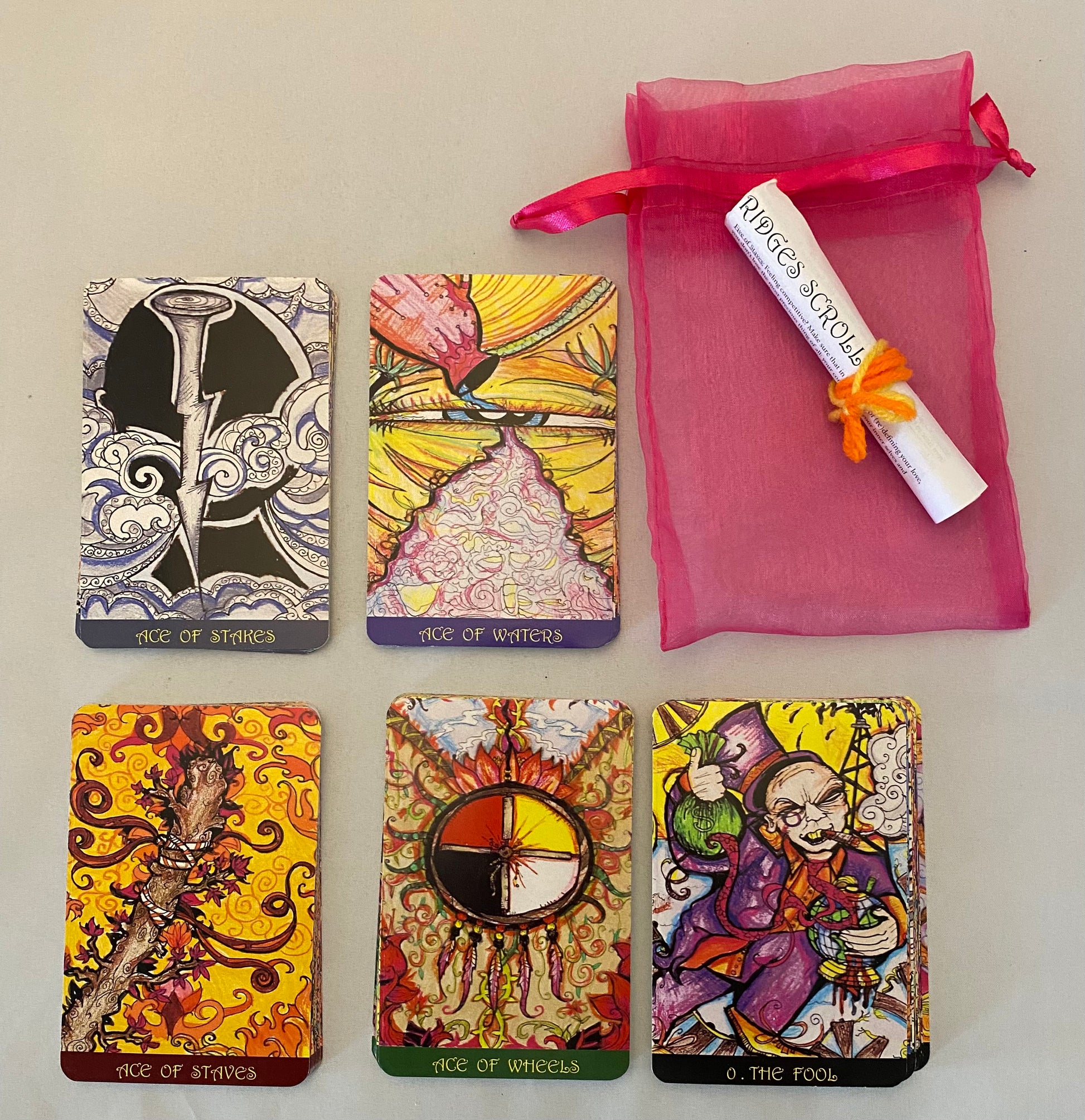 Collection of colorful tarot cards with a pink drawstring bag on a light surface.