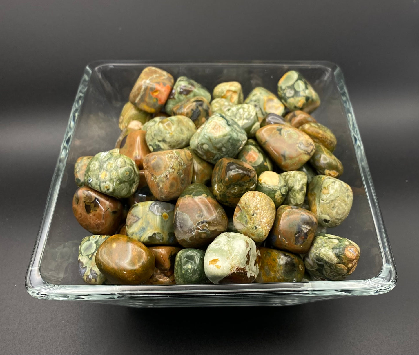 Collection of Rhyolite, green and brown, stones in a clear glass container on a dark background