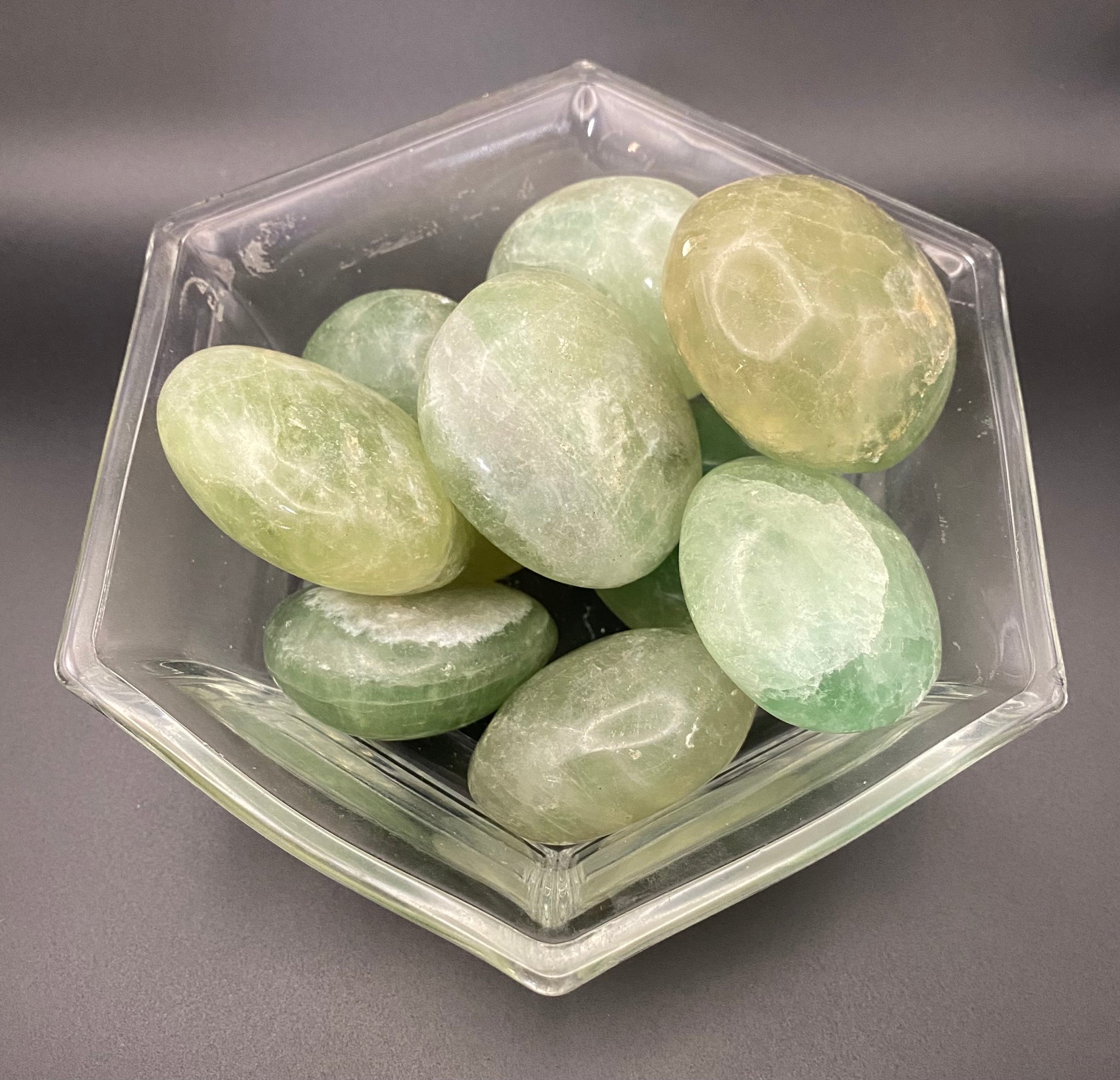Hexagonal container filled with green fluorite stones on a gray background
