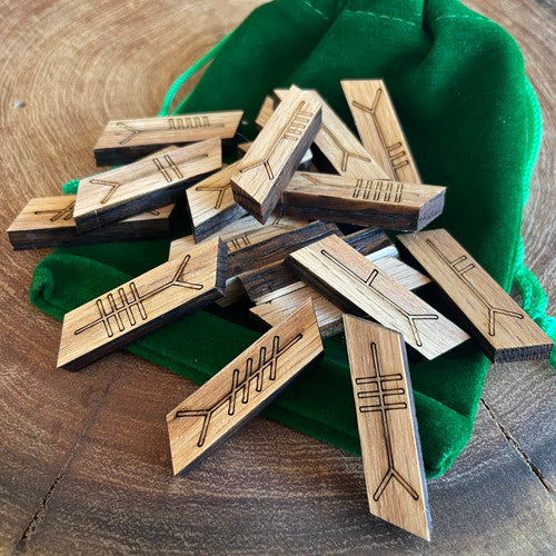 A collection of wooden Ogham stones with pouch on a wooden surface. The stones are inscribed with Ogham script.