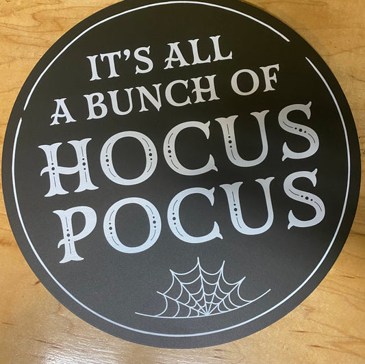 Round black sign with white text and spider web design on a wooden surface