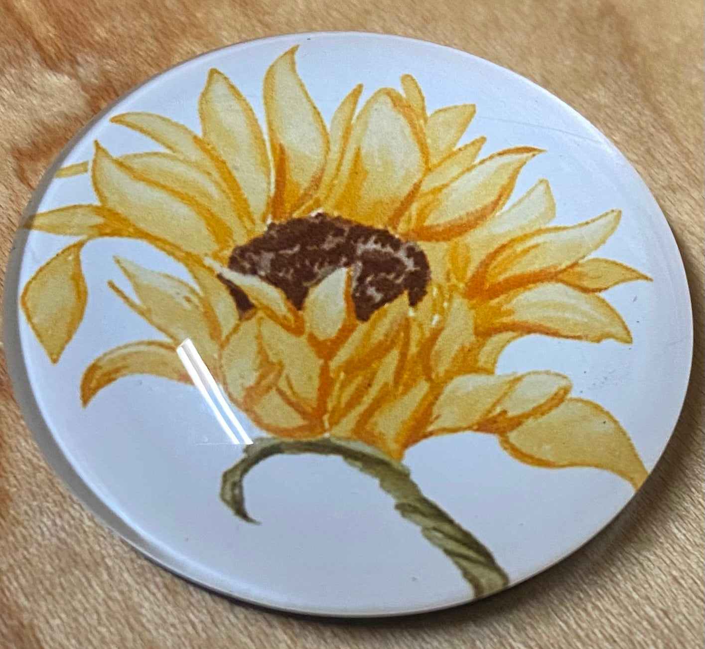 Round magnet with a sunflower design on a wooden surface