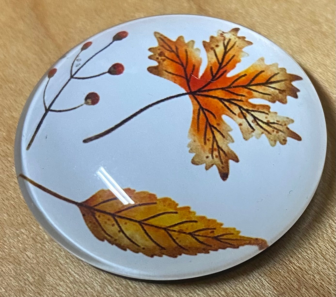 Round magnet with autumn leaf design on a wooden surface