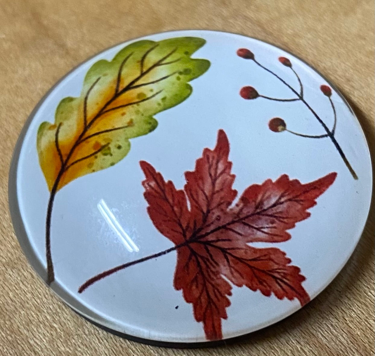 Round 
magnet with autumn leaf design on a wooden surface