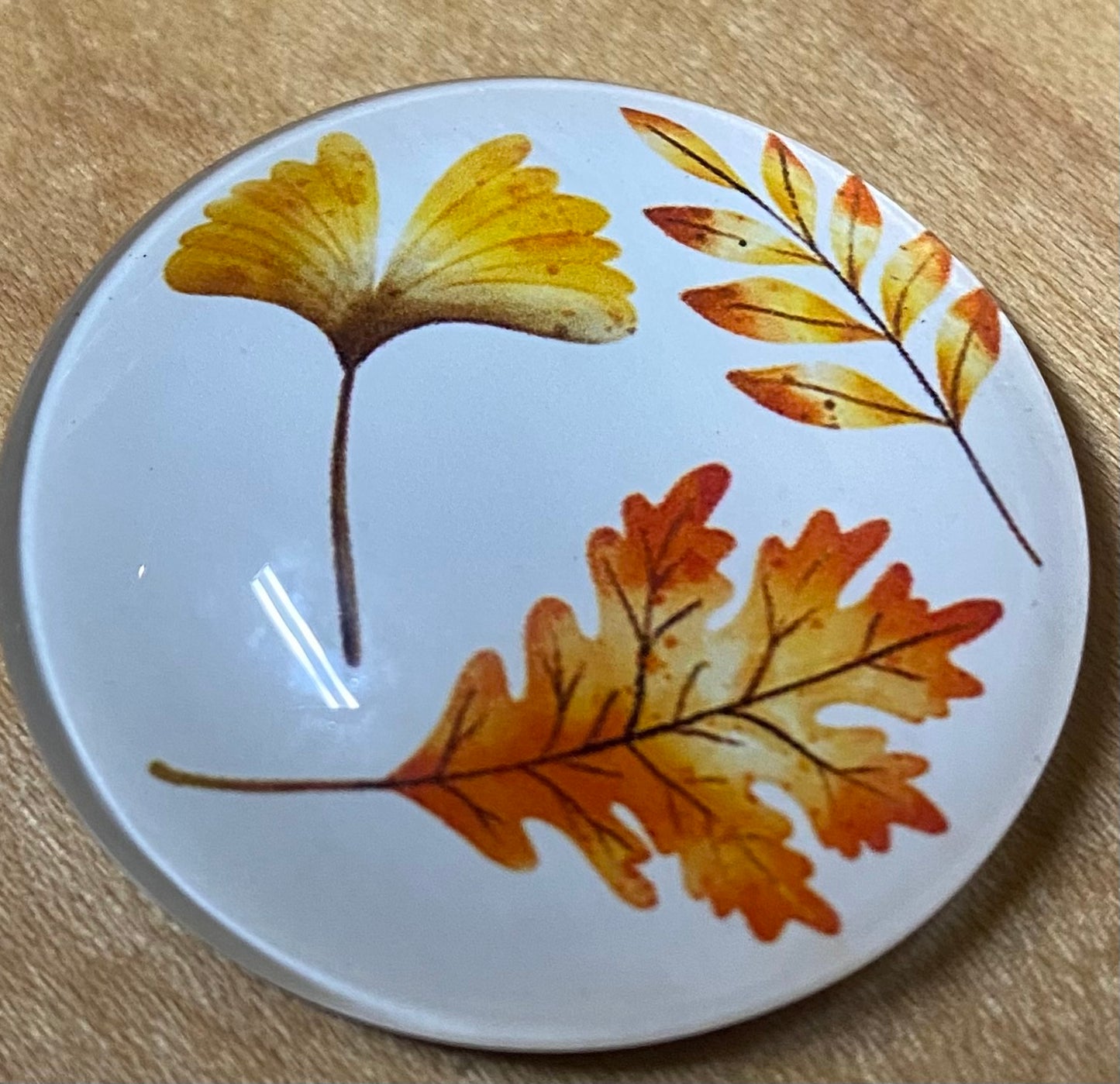 Round magnet with autumn leaf design on a wooden surface