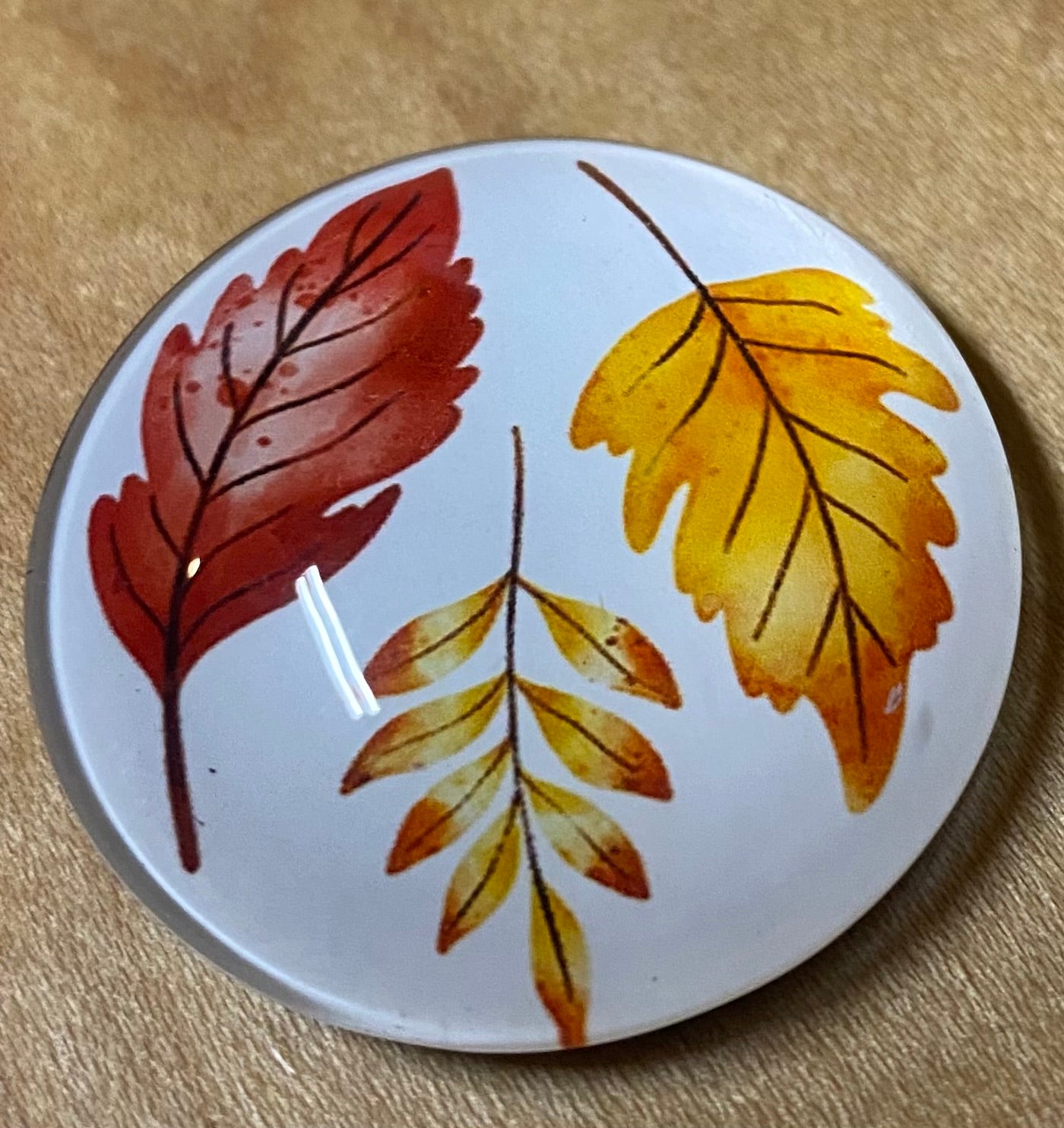 Round magnet with autumn leaf design on a beige surface
