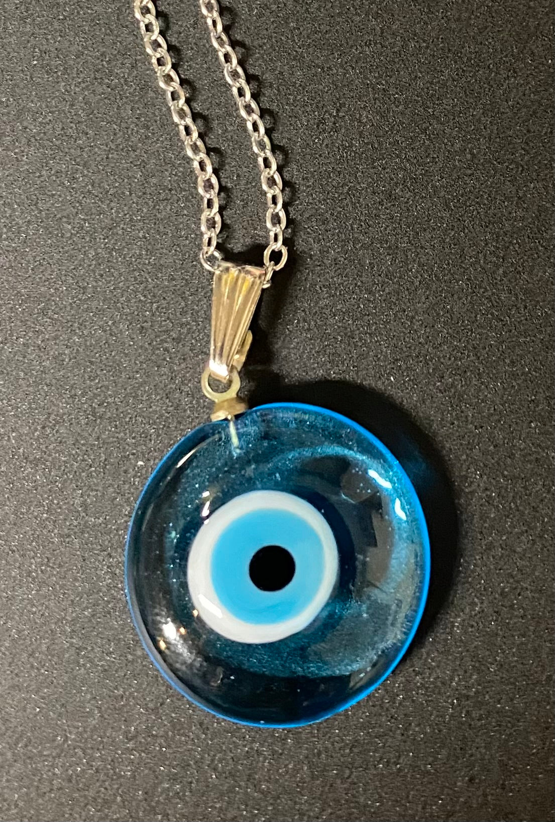 Blue evil eye pendant on a chain against a dark background