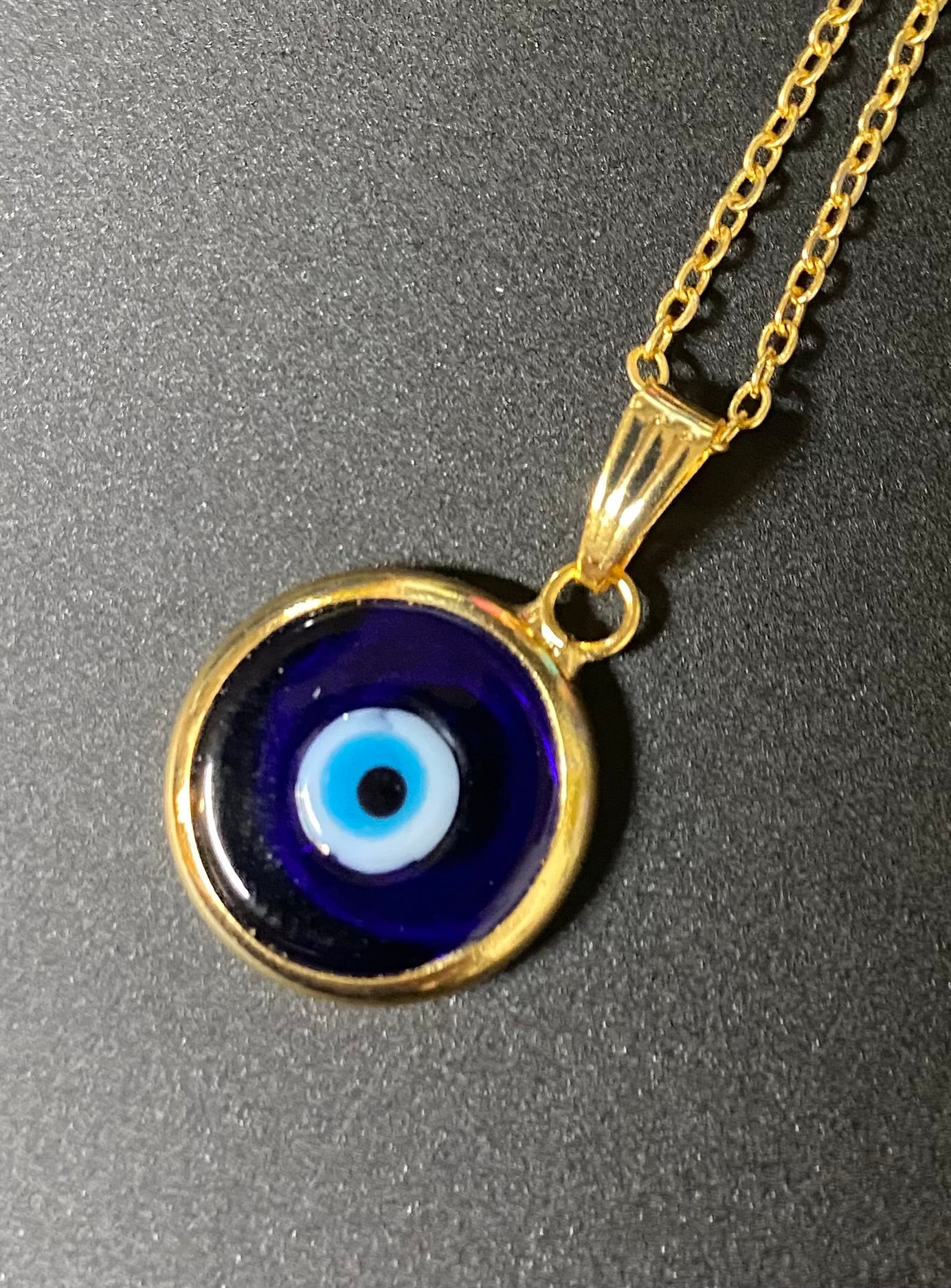 Gold necklace with a blue evil eye pendant on a gray background
