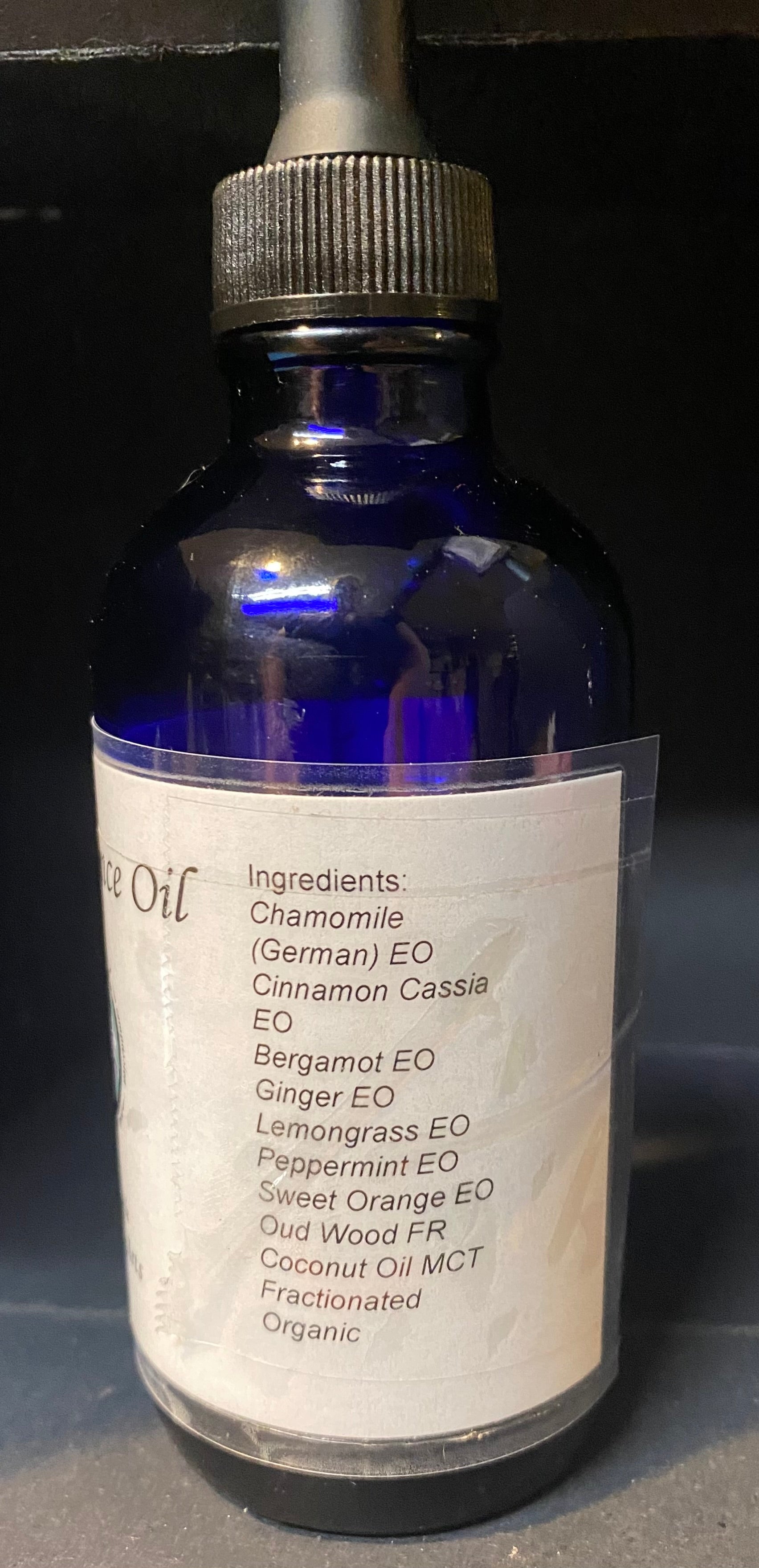 Blue glass bottle with dropper labeled 'Essential Oil' on a dark background