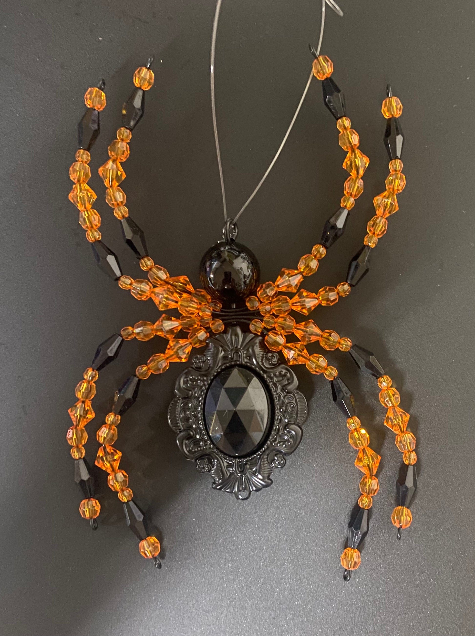Decorative spider with orange beads and a black center on a gray background