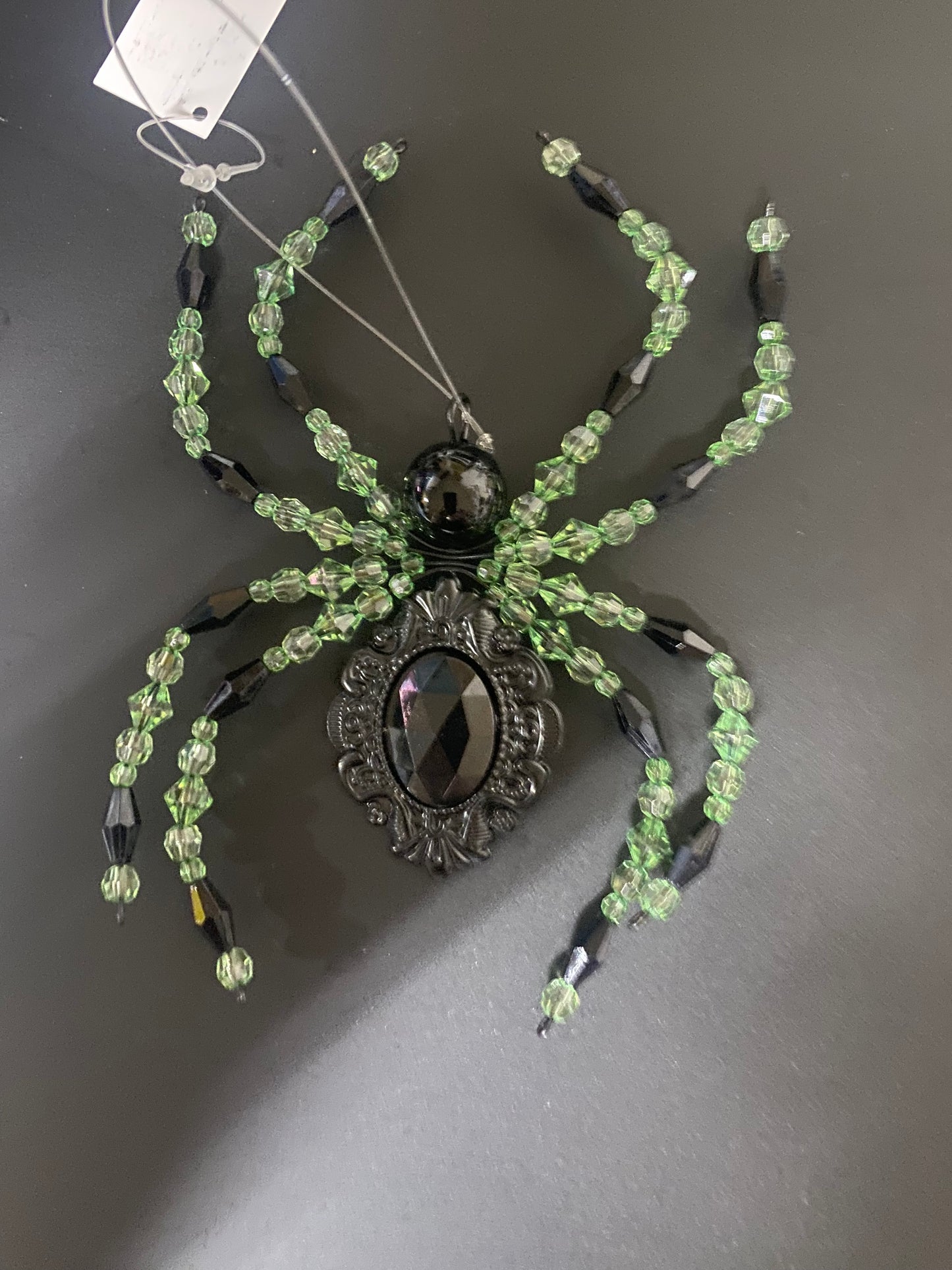 Decorative spider with green beads and a metallic center on a dark background