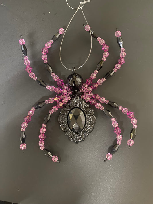 Spider-shaped decorative item with pink and black beads on a gray background