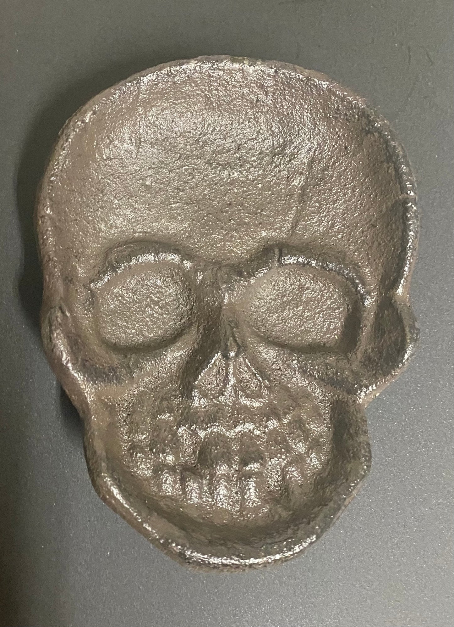 Metallic skull-shaped object on a gray background