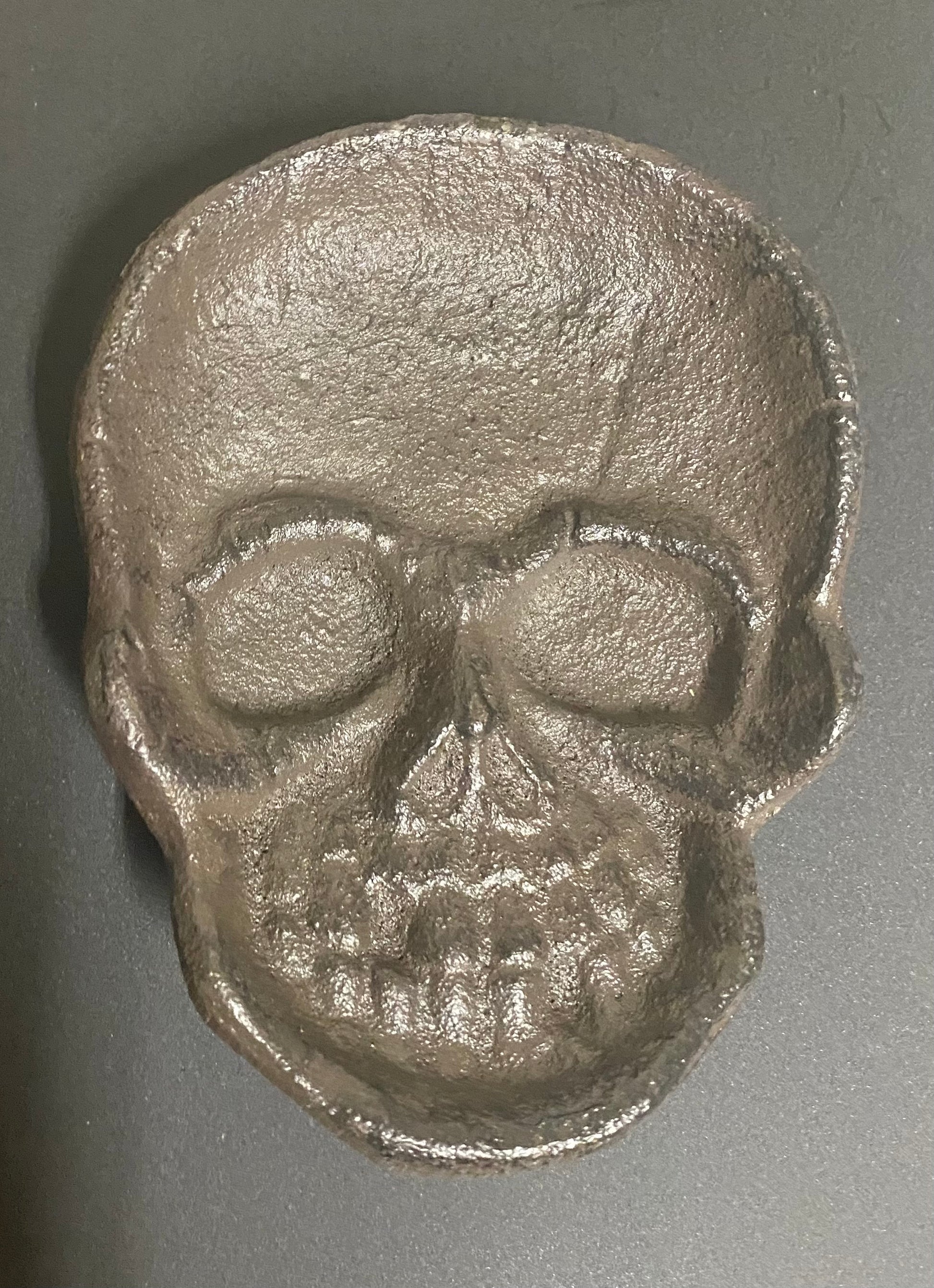 Metallic skull-shaped object on a gray background