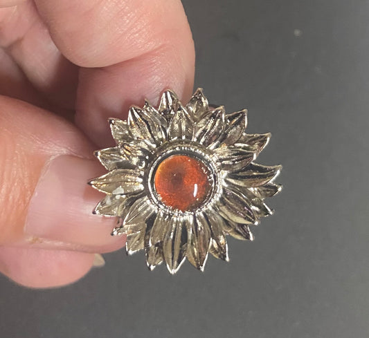 Silver sunflower-shaped Ring with a red center held between fingers against a dark background