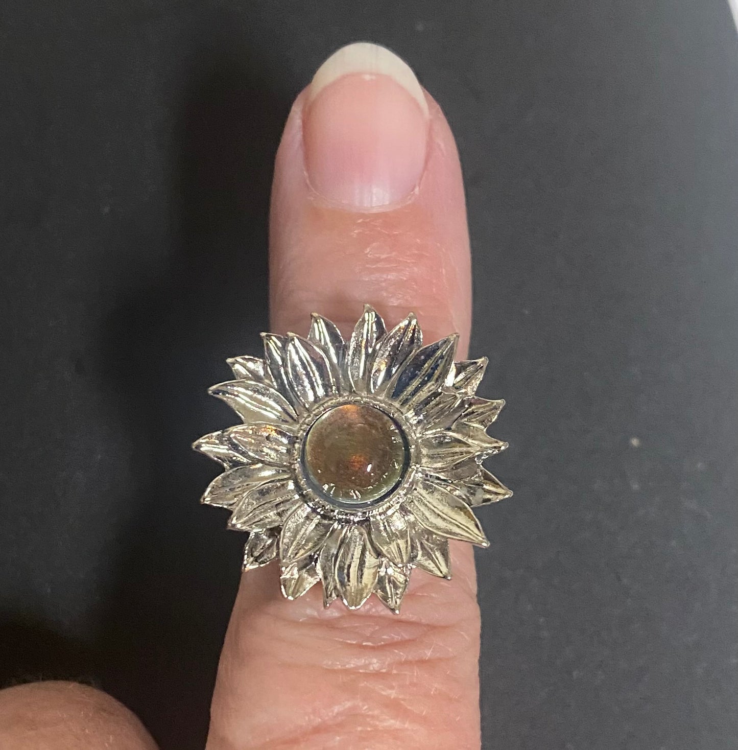 Silver sunflower-shaped ring on a finger against a dark background