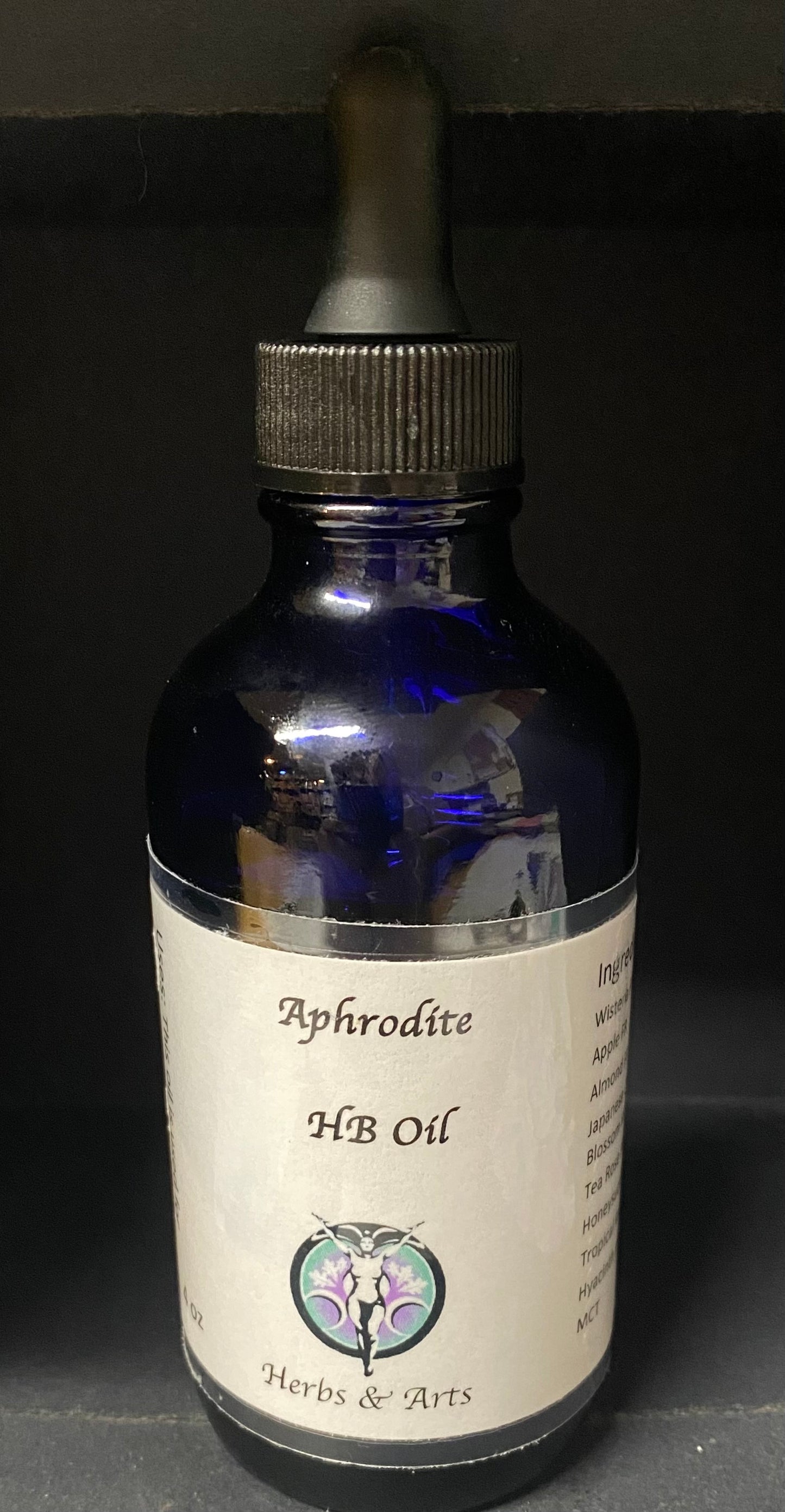 Blue glass bottle with dropper labeled 'Aphrodite HB Oil' on a dark background