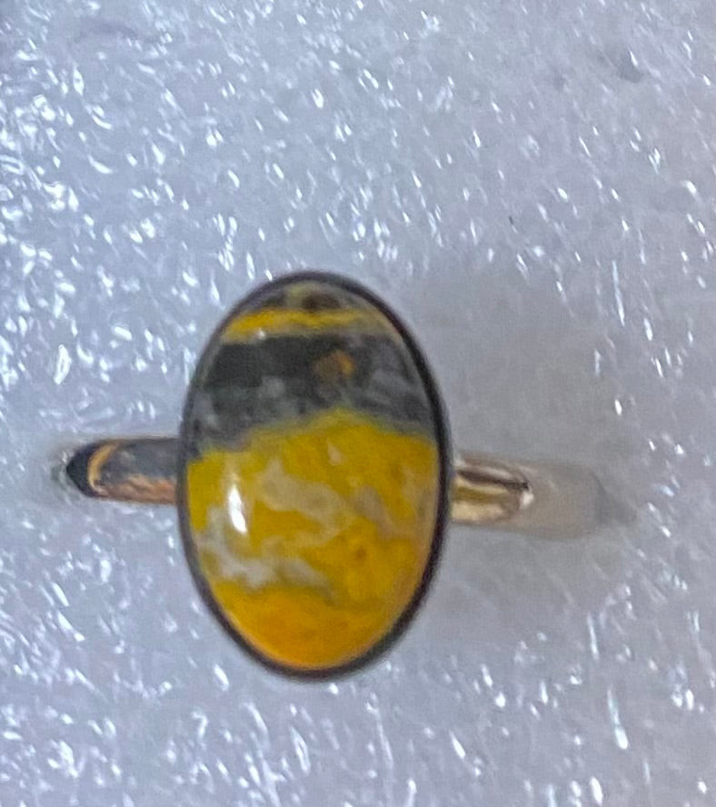 Ring with a yellow and gray oval stone on a textured white background