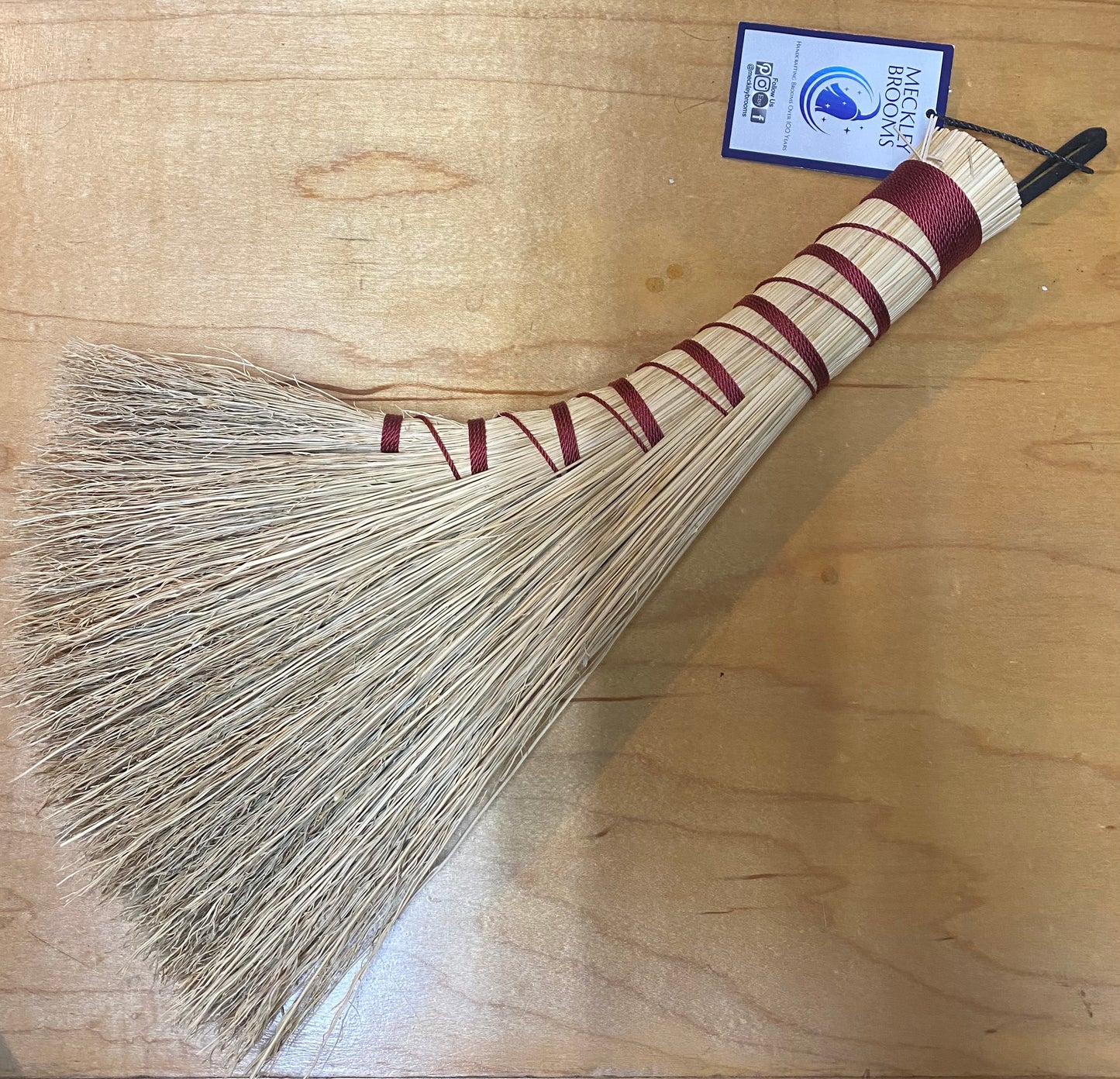 Broom with a striped handle on a wooden surface, featuring a brand label.