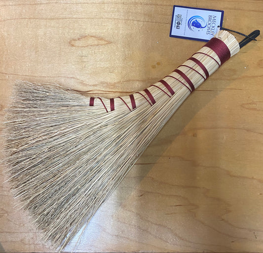 Broom with a striped handle on a wooden surface, featuring a brand label.