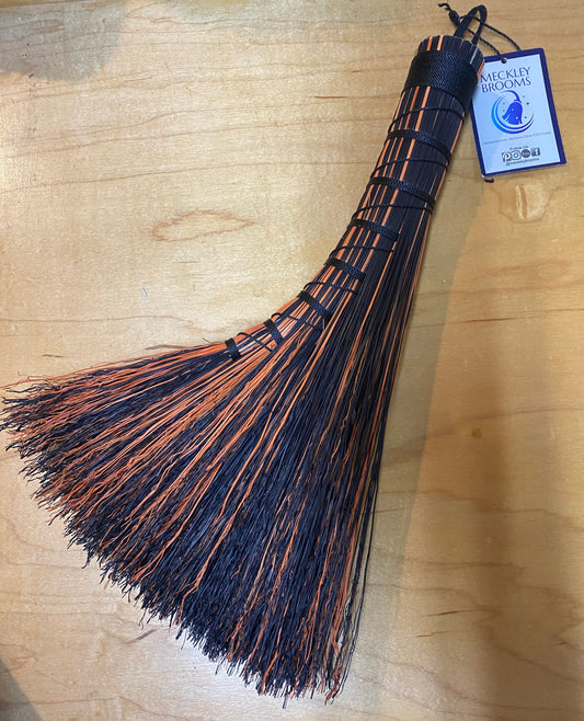 Black and orange broom with a Weckley Brooms tag on a wooden surface