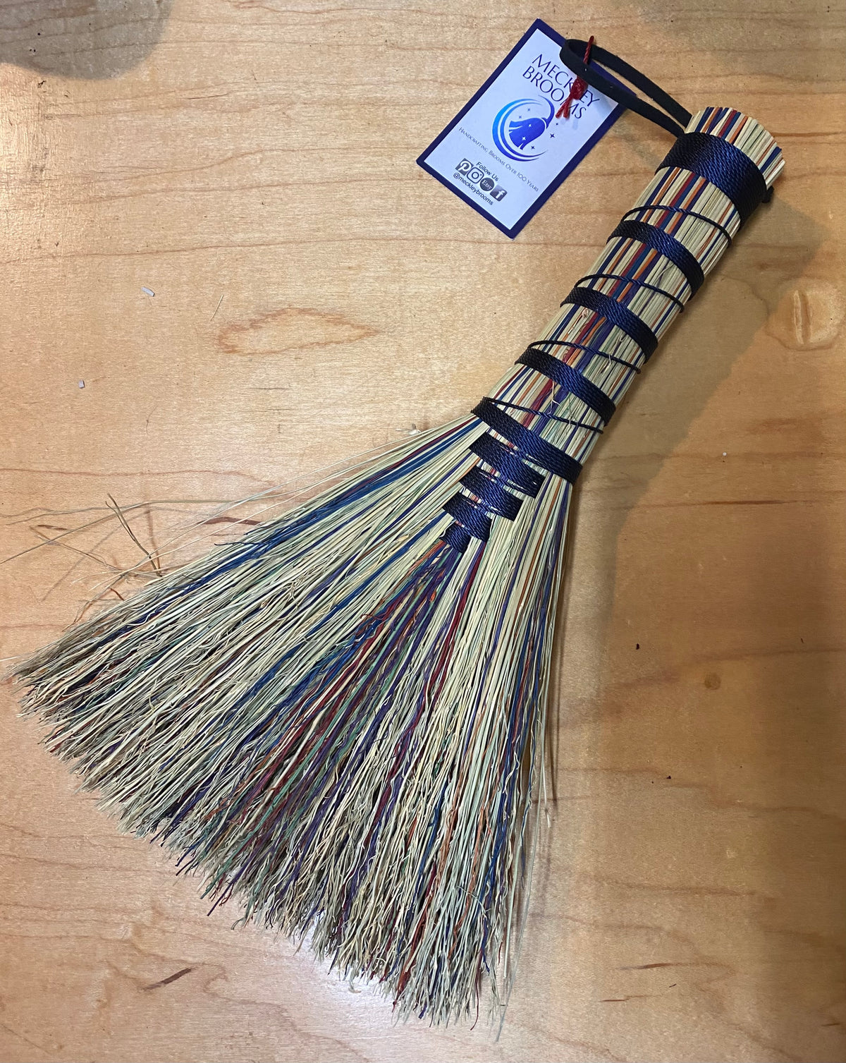 Broom with a blue handle and bristles on a wooden surface, featuring a label.