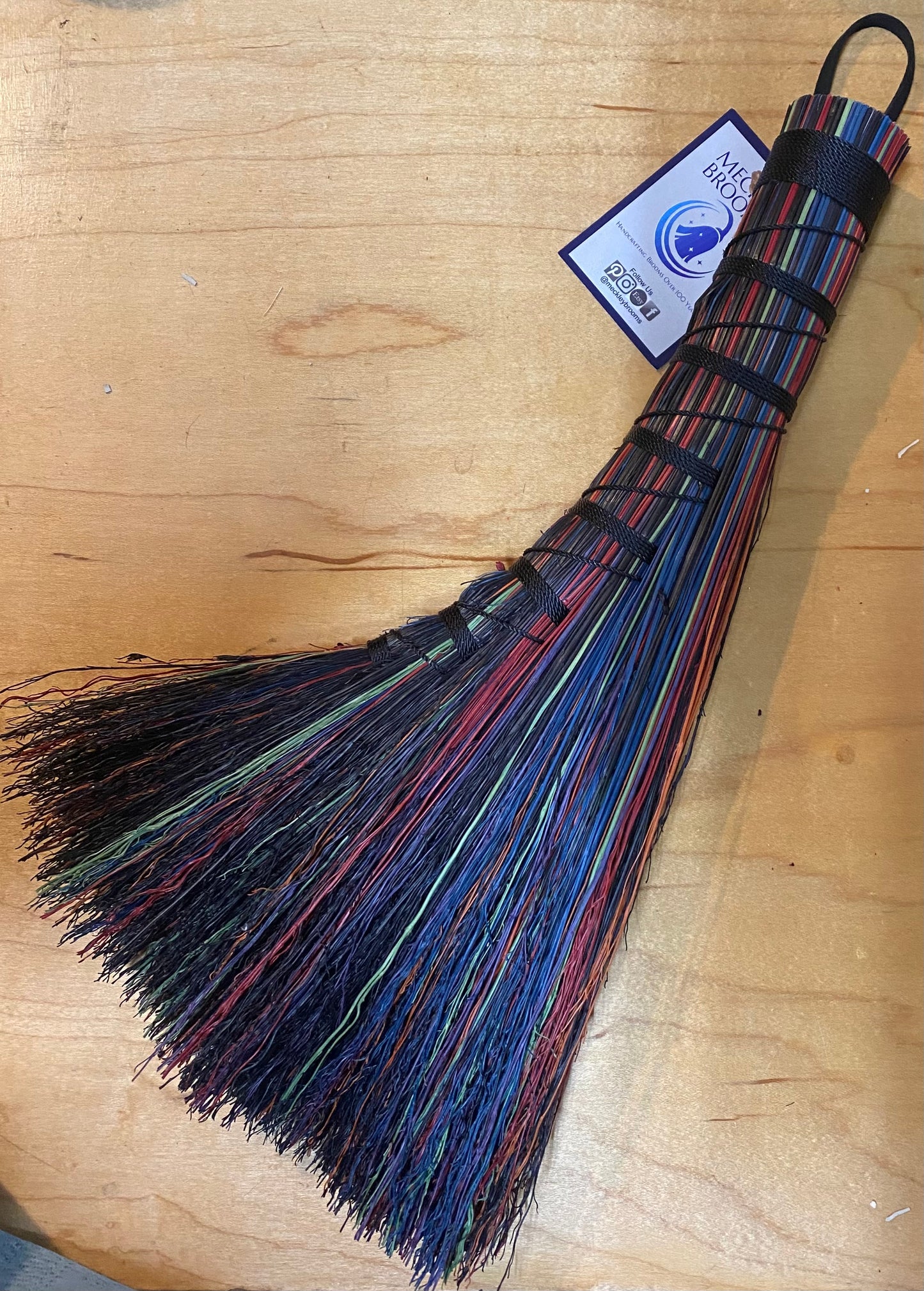 Multicolored broom on a wooden surface with a visible brand label.
